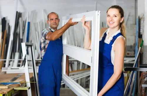 Junge Frau und Mann in Arbeitskleidung tragen einen weißen Fensterrahmen