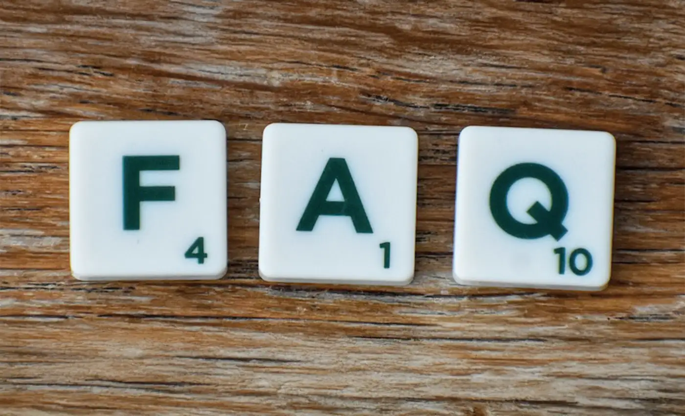 Die Buchstaben F A und Q auf Scrabble-Buchstaben, die auf einem Untergrund aus Holz liegen.