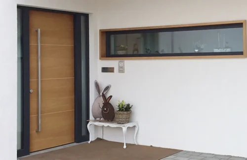 Eingangsbereich eines Hauses mit weißer Fassade, einer holzfarbenen Haustüre und eines Fensters mit Oster-Deko vor der Türe
