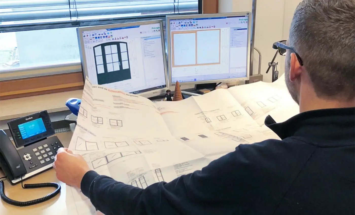 Mann hält eine Skizze mit mehreren Fenstern und vergleicht diese mit den Skizzen auf seinem Bildschirm.