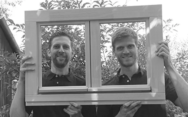 Zwei Männer von Team Englert schauen durch einen Fensterrahmen