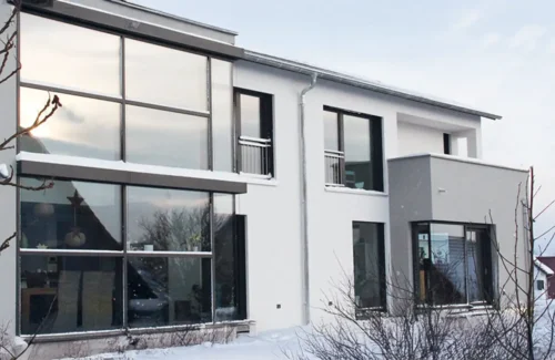 Blick durch den winterlichen Garten auf ein modernes Haus mit eindruckvoller Glasfassade